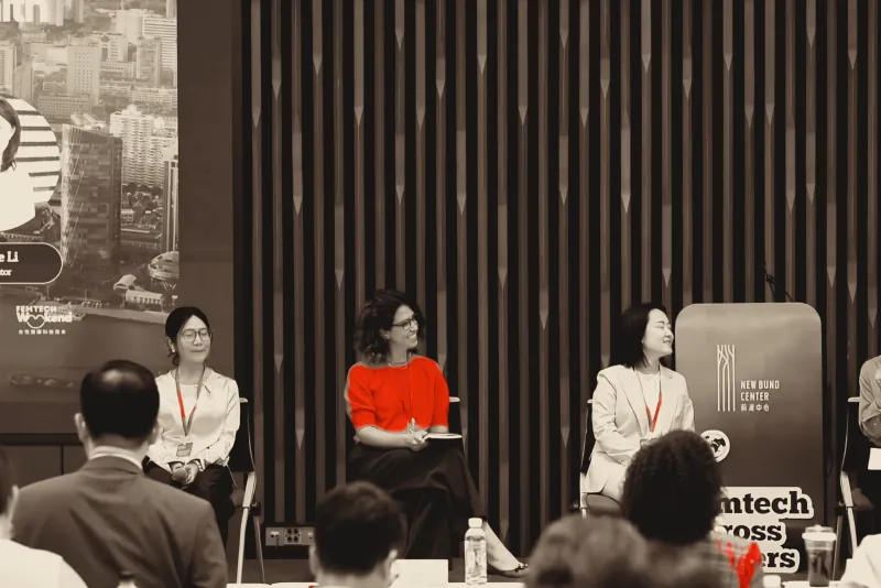 A panel of three speakers seated on stage, red lanyards and one red top the only colour in the room.