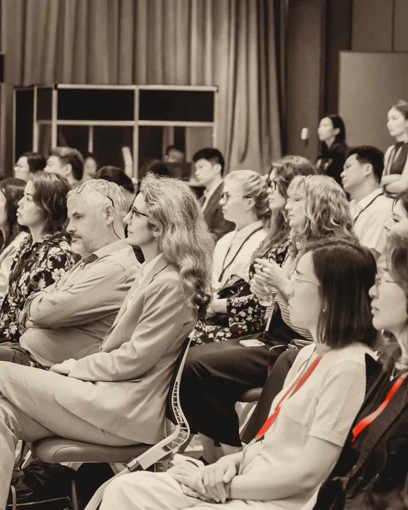 A full audience seated in rows, red lanyards visible among them.